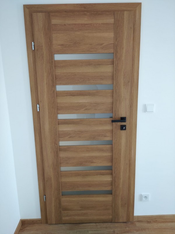 El tirador SULLA en color negro combina perfectamente con la puerta de madera — realización en Bélgica en Bruselas